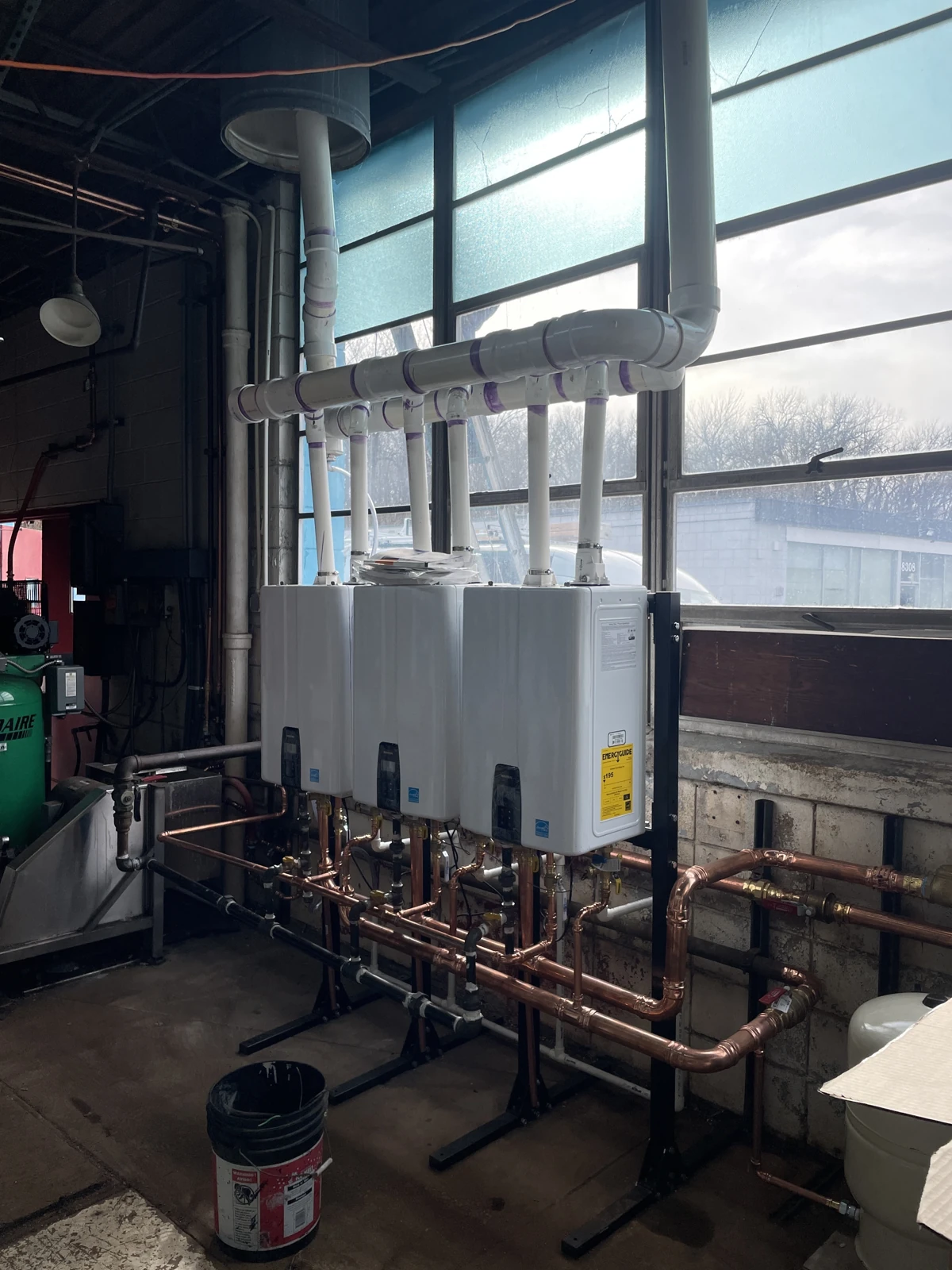 Mechanical equipment connected to copper pipework below and white vent piping above, shown from another angle.