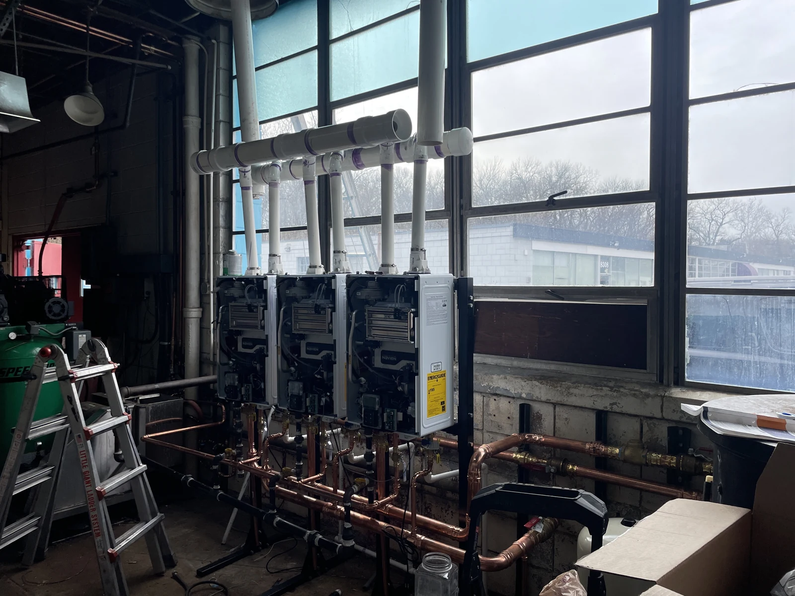Mechanical equipment with connected copper pipework and overhead venting beside large windows.